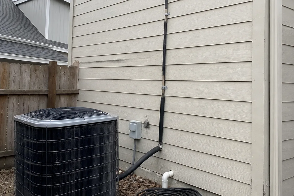 An outdoor condenser unit next to a house wall, refrigerant lines running up toward the attic where the matching indoor coil sits.