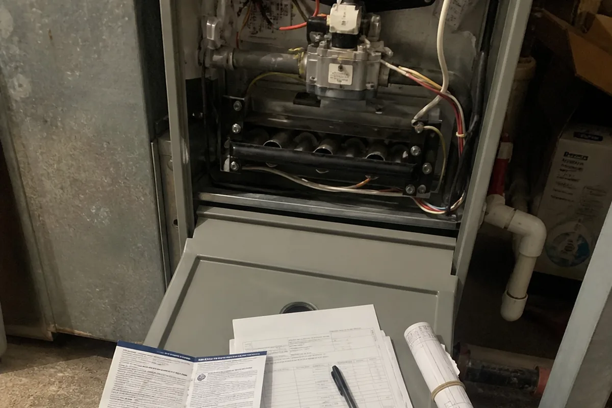 A folded manufacturer warranty registration card and installation paperwork resting on a furnace access panel.