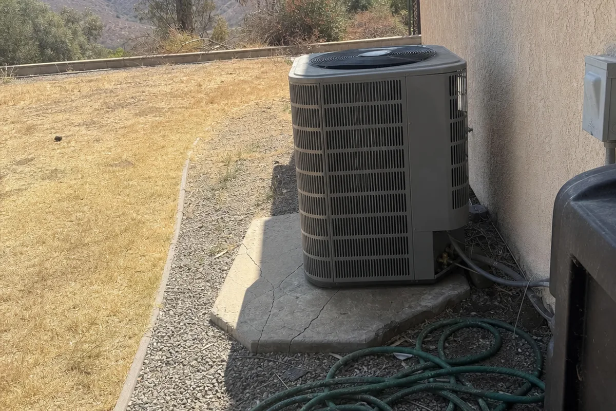 A residential condenser unit beside a stucco wall in an inland San Diego backyard under hard afternoon sun.