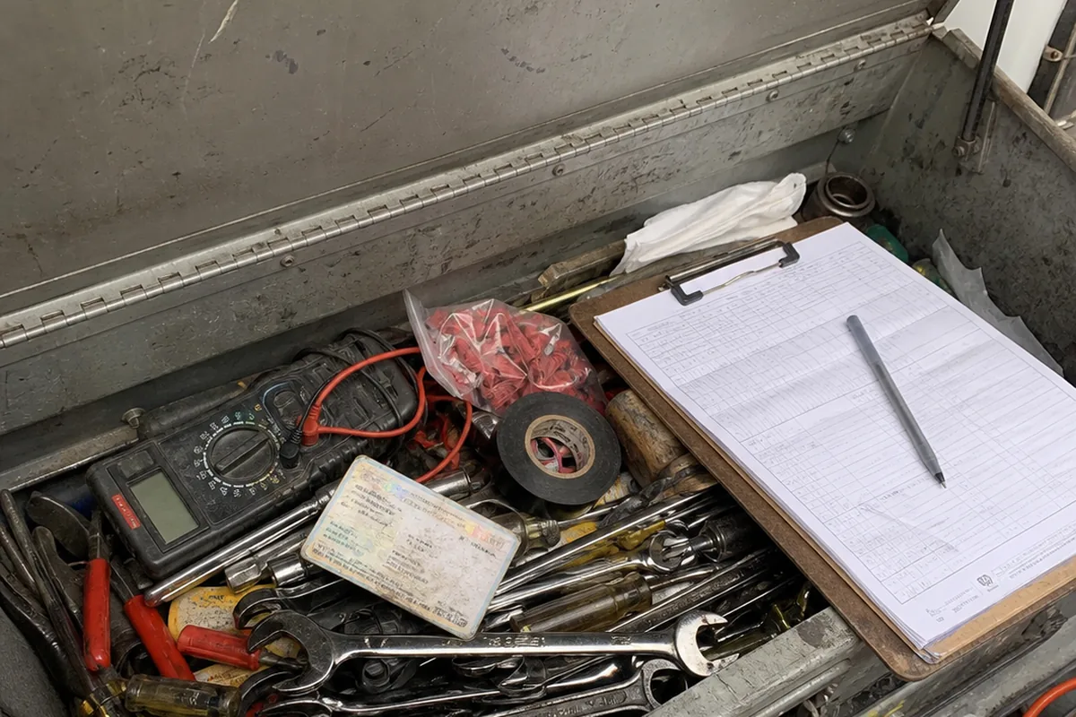 A laminated technician certification card resting on a service van's toolbox next to a work order clipboard.