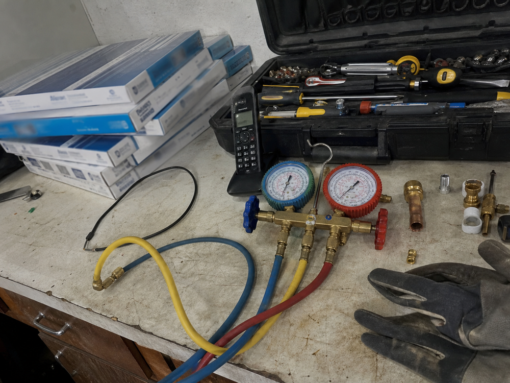 An HVAC workbench with manifold gauges, tools, and an office phone.