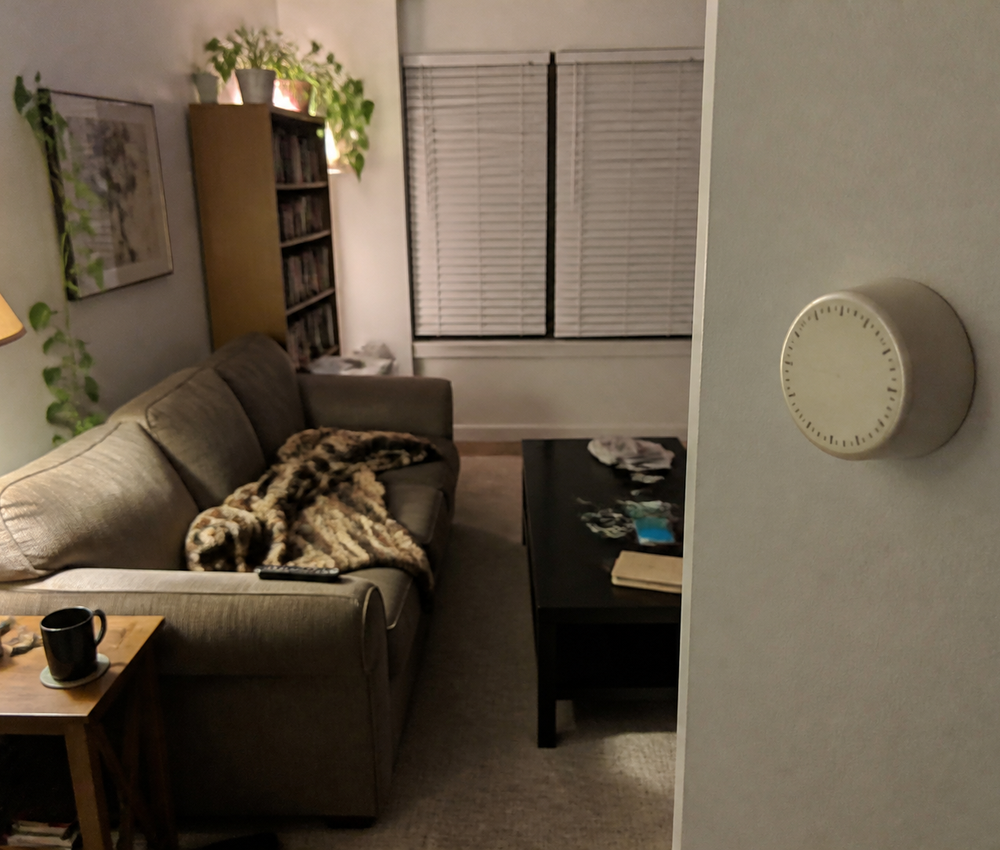 A cozy living room in the evening with a round thermostat on the wall.